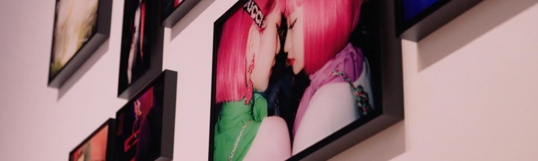 View of photographs mounted on a wall in black frames, including a photograph of two women with pink hair