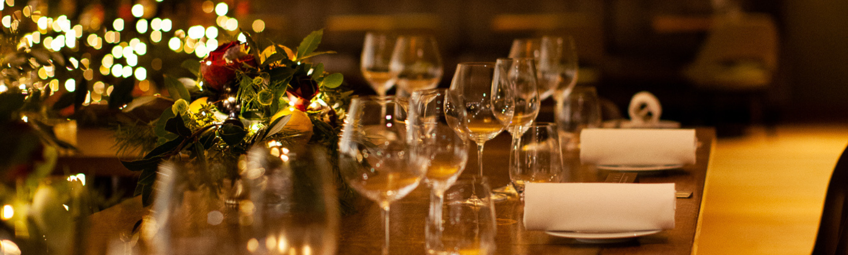 Image of a table laid out for a Christmas dinner party with glasses, winter flowers and Christmas lights in the background