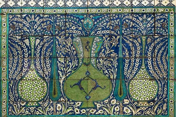 Mosaic of small blue, green and yellow tiles forming a picture of vases and trees amid flowers