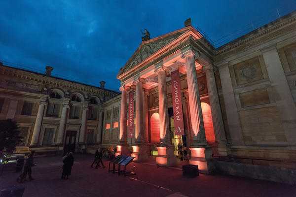 The stone front of the Ashmolean Museum, lit up with red and white lights, against a dark blue sky