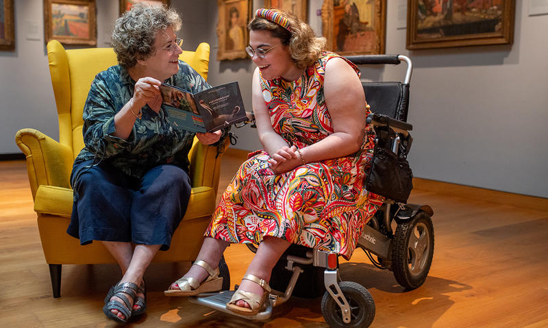 Visitors sitting together in gallery, one woman is smiling and chatting with her friend in a wheelchair 