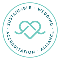 A teal blue logo of a heart on white background with the words 'Sustainable Wedding Alliance Accreditation' around the circumference